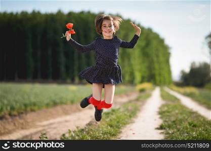Little girl jumping in nature field wearing beautiful dress with flowers in her hand.