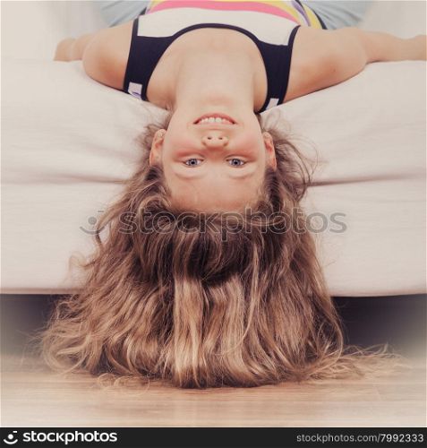 Little girl kid with long hair upside down on sofa. Happy little girl with long hair lying upside down on sofa at home. Kid playing having fun on couch.