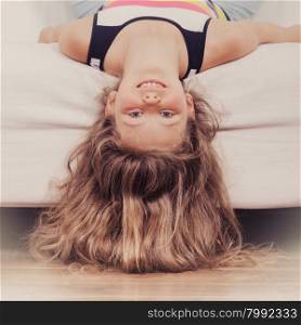 Little girl kid with long hair upside down on sofa. Happy little girl with long hair lying upside down on sofa at home. Kid playing having fun on couch.
