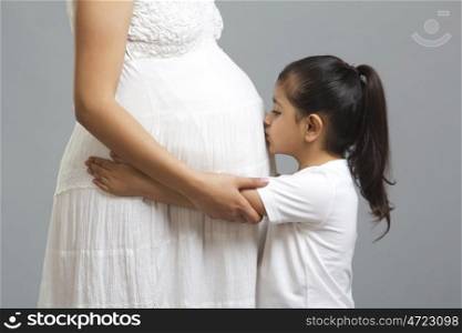 Little girl kissing stomach of pregnant mother