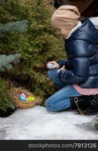 Little girl kneeling next to tree and picking Easter egg