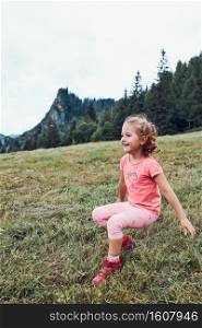 Little girl laying playing on grass enjoying summer day. Happy child playing in the field during vacation trip in mountains. Mountain landscape in the background. Little girl laying playing on grass enjoying summer day during vacation trip