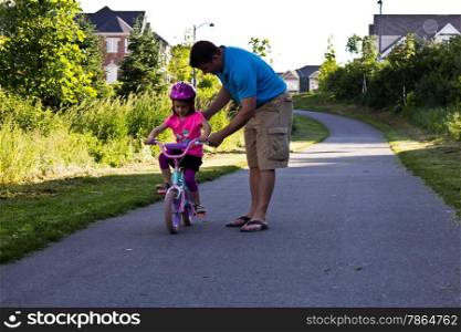 Little girl learning how to ride a bike with her father