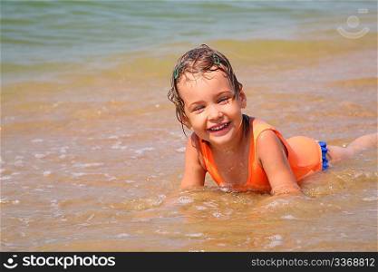 Little girl lies in waves on shore