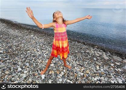 little girl lifted hands upwards on stony beach