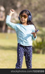 Little girl listening to music on the smartphone with her headphones in the park