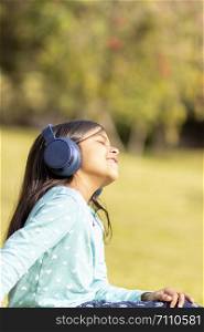 Little girl listening to music on the smartphone with her headphones in the park