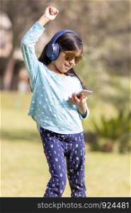 Little girl listening to music on the smartphone with her headphones in the park