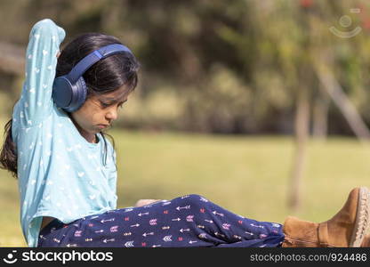 Little girl listening to music on the smartphone with her headphones in the park