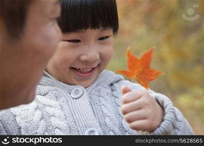 Little girl looking at leaf with her father, close-up, autumn