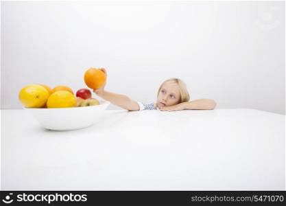 Little girl looking at orange while leaning on table