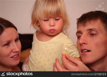 little girl looks on burning candle in father`s hand