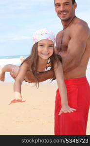 little girl lying down on father&rsquo;s arms on the beach