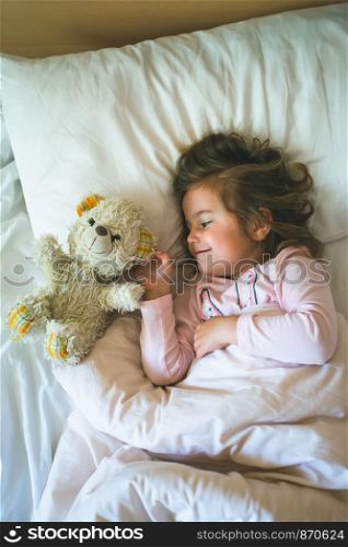 Little girl lying in a bed with teddy bear at the morning