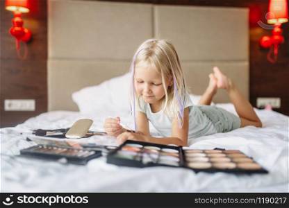 Little girl lying in bed and play with moms makeup at home. A truly carefree childhood, happy time