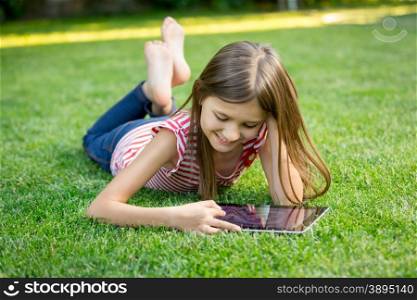 Little girl lying on grass and using tablet