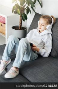 Little girl  lying on the couch with an electronic tablet listens to music in white headphones. Using wireless devices for education.