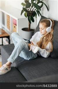 Little girl  lying on the couch with an electronic tablet listens to music in white headphones. Using wireless devices for education.