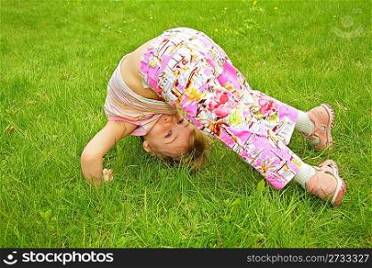 little girl makes exercise on grass