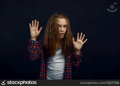 Little girl makes face leaning against the glass in studio. Happy childhood, children having fun, funny kid isolated on dark background. Little girl makes face leaning against the glass