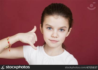 Little Girl making a call me gesture, against background of burgundy wall