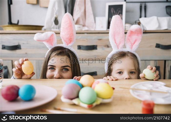 little girl mother bunny ears hiding table with colored eggs