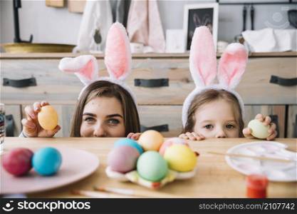 little girl mother bunny ears hiding table with colored eggs