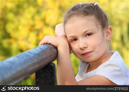 little girl on a bridge in early fall park is looking at camera