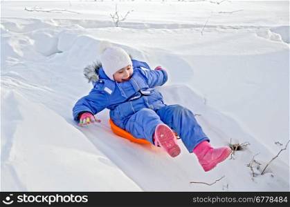 Little girl on a sled sliding down a hill in the snow in winter