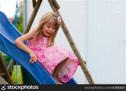 Little girl on slide in summer in the garden playground