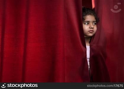 Little girl peeking out from a curtain