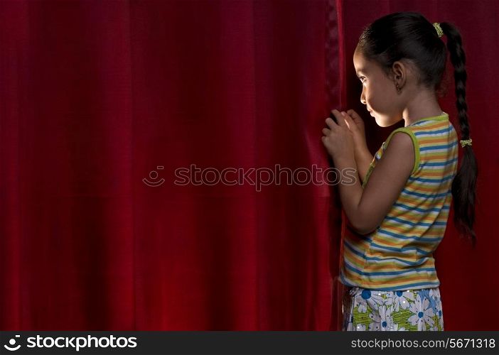 Little girl peeking out from behind a curtain