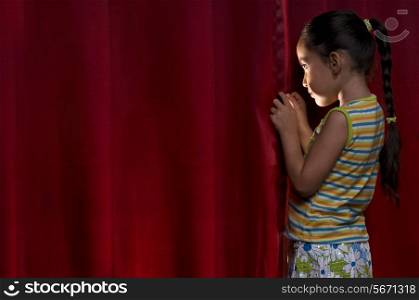 Little girl peeking out from behind a curtain