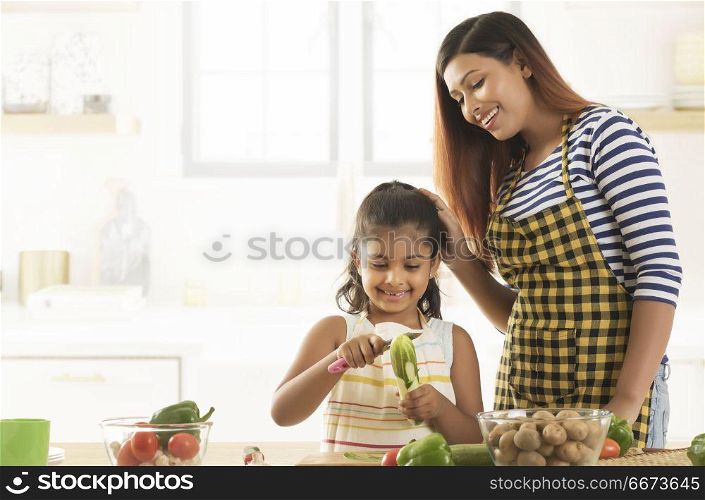 Little girl peeling cucumber and mother watching her