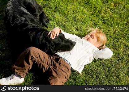 Little girl petting her dog laying on a green lawn