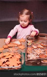 Little girl placing Christmas gingerbread cookies on wooden tray