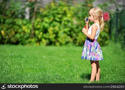 little girl play with bubble blower on green lawn