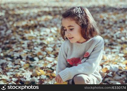 Little girl playing in a city park in autumn, wearing pants and jersey with a hairpin in hair