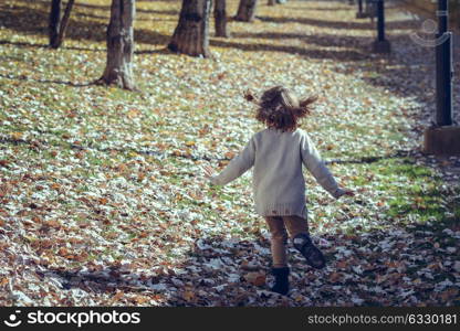 Little girl playing in a city park in autumn, wearing pants and jersey with a hairpin in hair