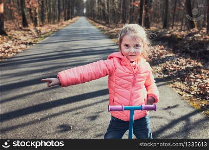 Little girl playing in the park, riding a scooter, having fun on sunny autumn day. Real people, authentic situations