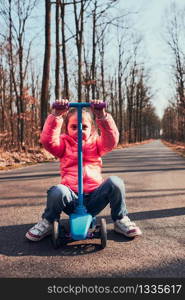 Little girl playing in the park, riding a scooter, having fun on sunny autumn day. Real people, authentic situations