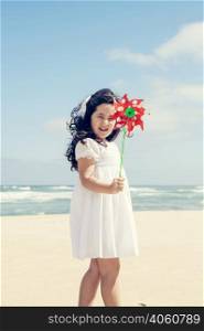 Little girl playing on the beach with a pinwheel