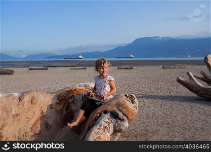 Little girl playing on wood sculpture on beach, Vancouver, British Columbia, Canada