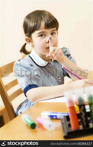 little girl playing with colors and having a finger on her lips for silence