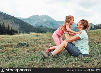 Little girl playing with her mother on grass enjoying summer day. Happy family playing in the field during vacation trip in mountains. Little girl playing with her mother on grass enjoying summer day during vacation trip in mountains