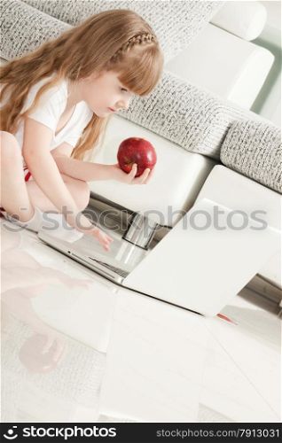 Little Girl Playing with Laptop and Eating an Apple