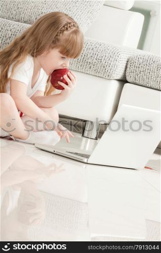 Little Girl Playing with Laptop and Eating an Apple