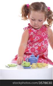 Little girl playing with model teapot and mugs