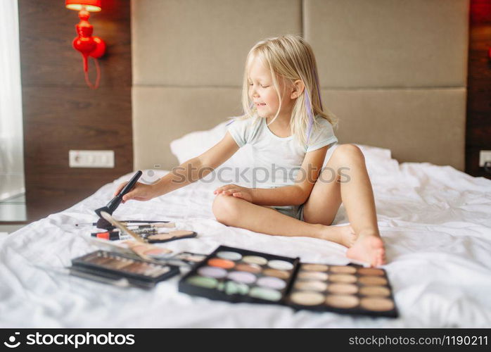 Little girl playing with moms makeup in bedroom at home. A truly carefree childhood, happy time