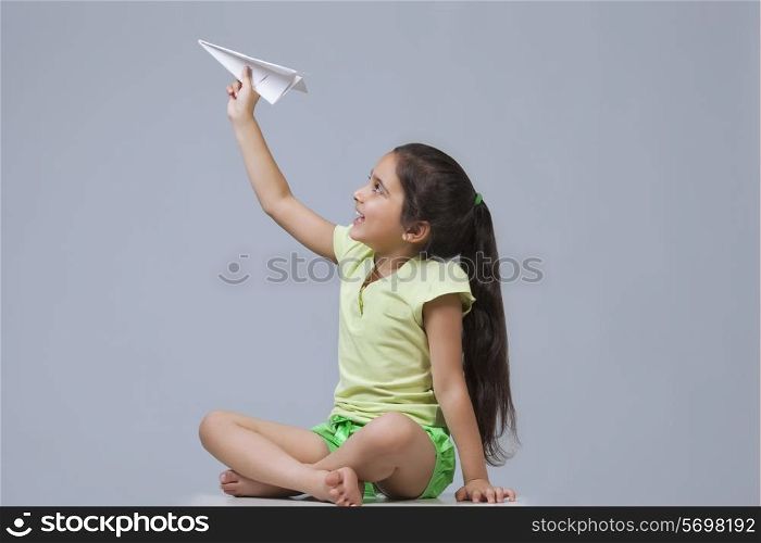 Little girl playing with paper airplane isolated over blue background